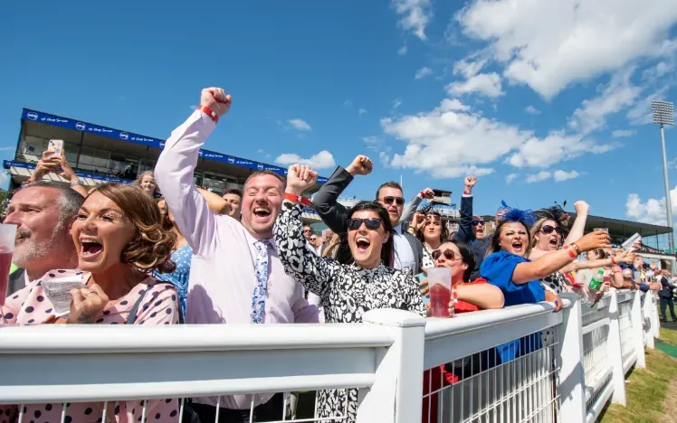 The crowd at the trackside at newcastle cheer the race in the sunshine