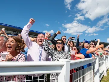 The crowd at the trackside at newcastle cheer the race in the sunshine