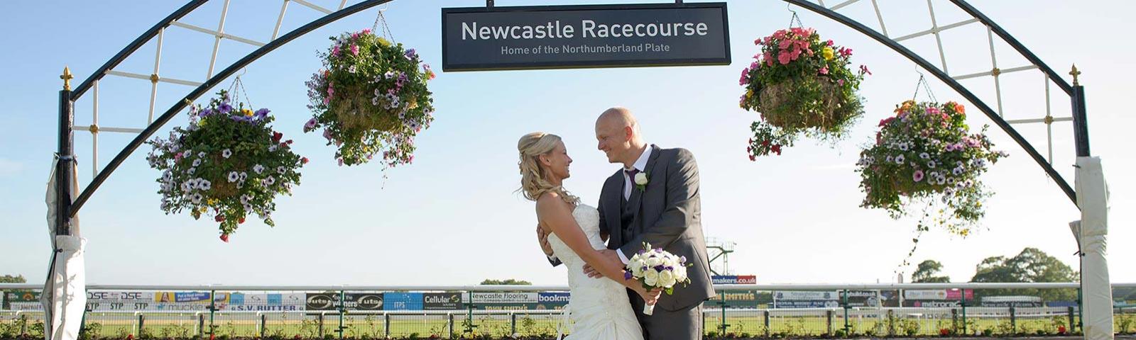 Bride and Groom embrace beneath a decorative Arch on their Wedding day at Newcastle Racecourse