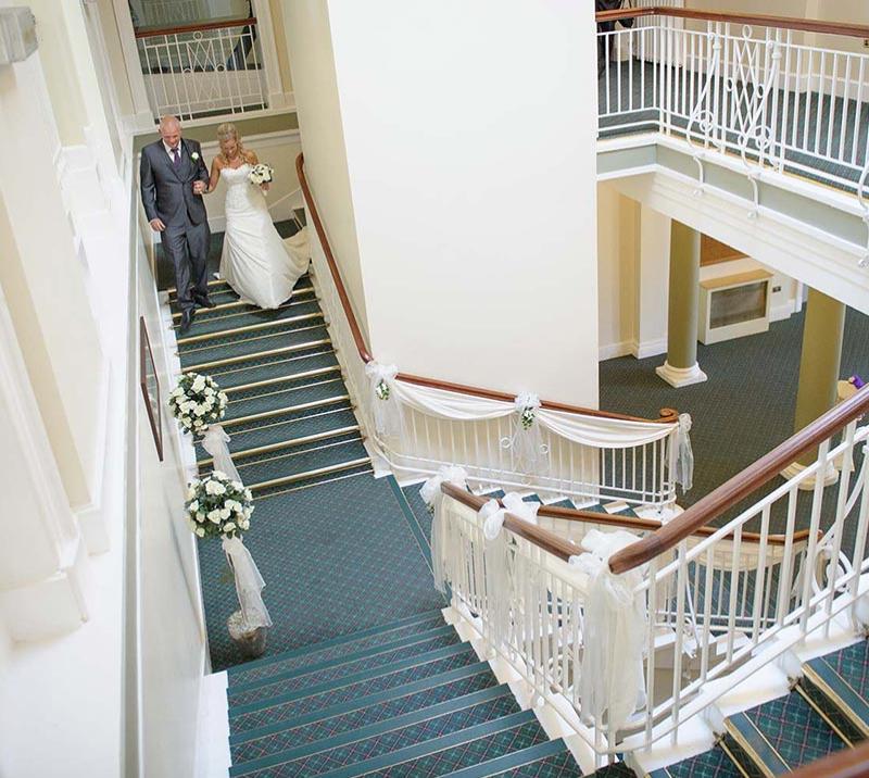 A bride is walked downstairs by her father on route to the ceremony.